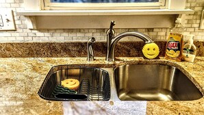 Una cocina con un lavamanos doble, una ventana sobre el lavamanos y una encimera con un escurreplatos.