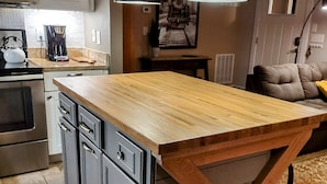 Una cocina con isla de madera, armarios grises, cafetera e iluminación colgante.