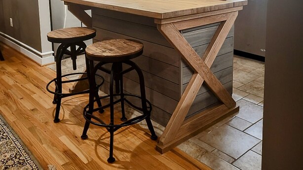 Una cocina con una isla de madera, dos taburetes e iluminación colgante.