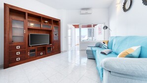A living room with a large wooden entertainment unit, a blue sofa, and a flat-screen TV. - Casa el Varadero - Pool and Gym By LVH (Puerto del Carmen)