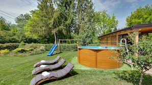 Een achtertuin met een houten jacuzzi, een blauwe glijbaan en ligstoelen.