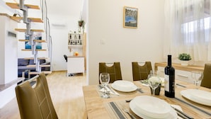 Een eetgedeelte met een houten tafel voor vier personen, een wijnfles en een schilderij aan de muur.
