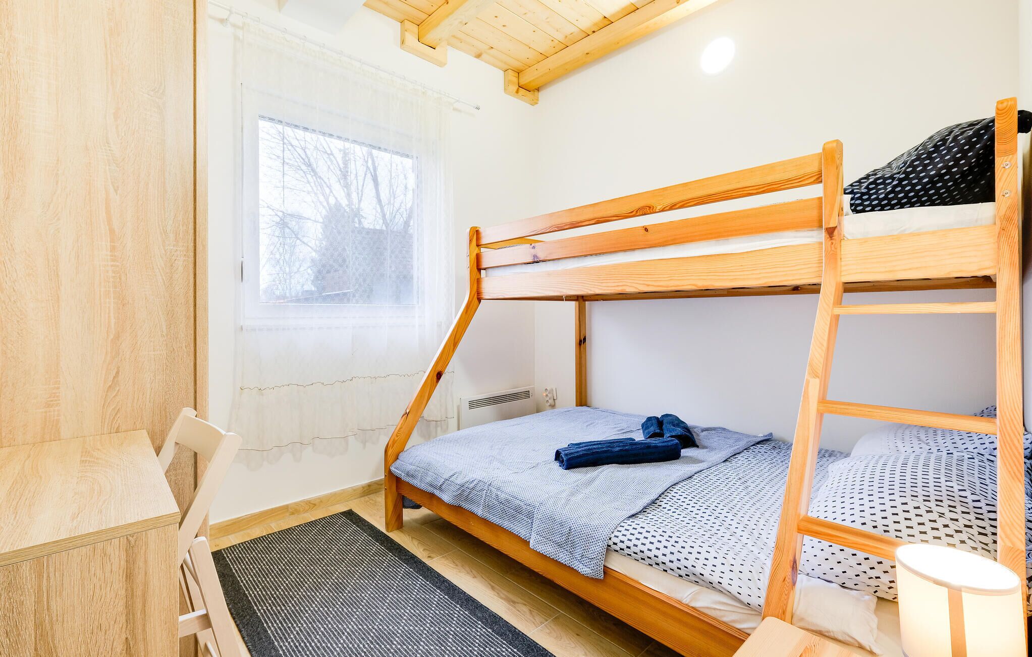 A bunk bed room with a window, a desk, and a chair.