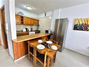 Cocina compacta con armarios de madera, un refrigerador de acero inoxidable y una mesa de comedor preparada para cuatro comensales.