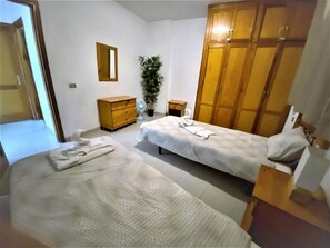 Un dormitorio con dos camas, un armario, una mesita de noche, un espejo y una planta en maceta.