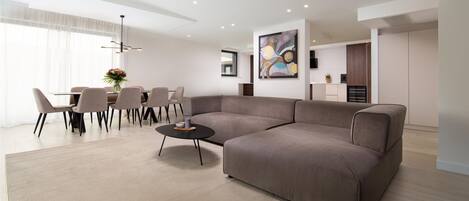 Ein modernes Wohnzimmer mit einer Eckcouch, einem Essbereich mit Stühlen und einem Tisch sowie einer Küche im Hintergrund.