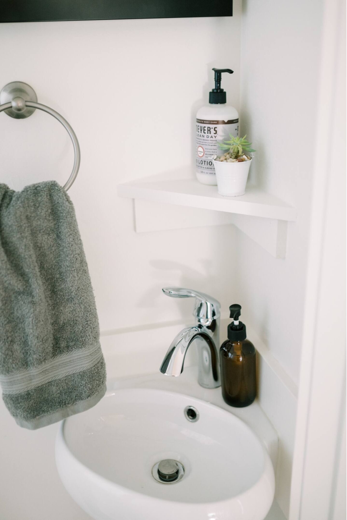 A bathroom with a white sink, a towel ring, a shelf with toiletries, and a small potted plant.