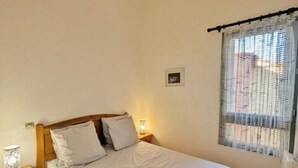 Un dormitorio con cama de madera, una mesita de noche, una lámpara y un ventanal con cortina.