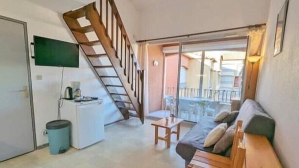 Un espacio habitable compacto con una escalera de madera, un sofá, una mesita y un televisor montado en la pared.