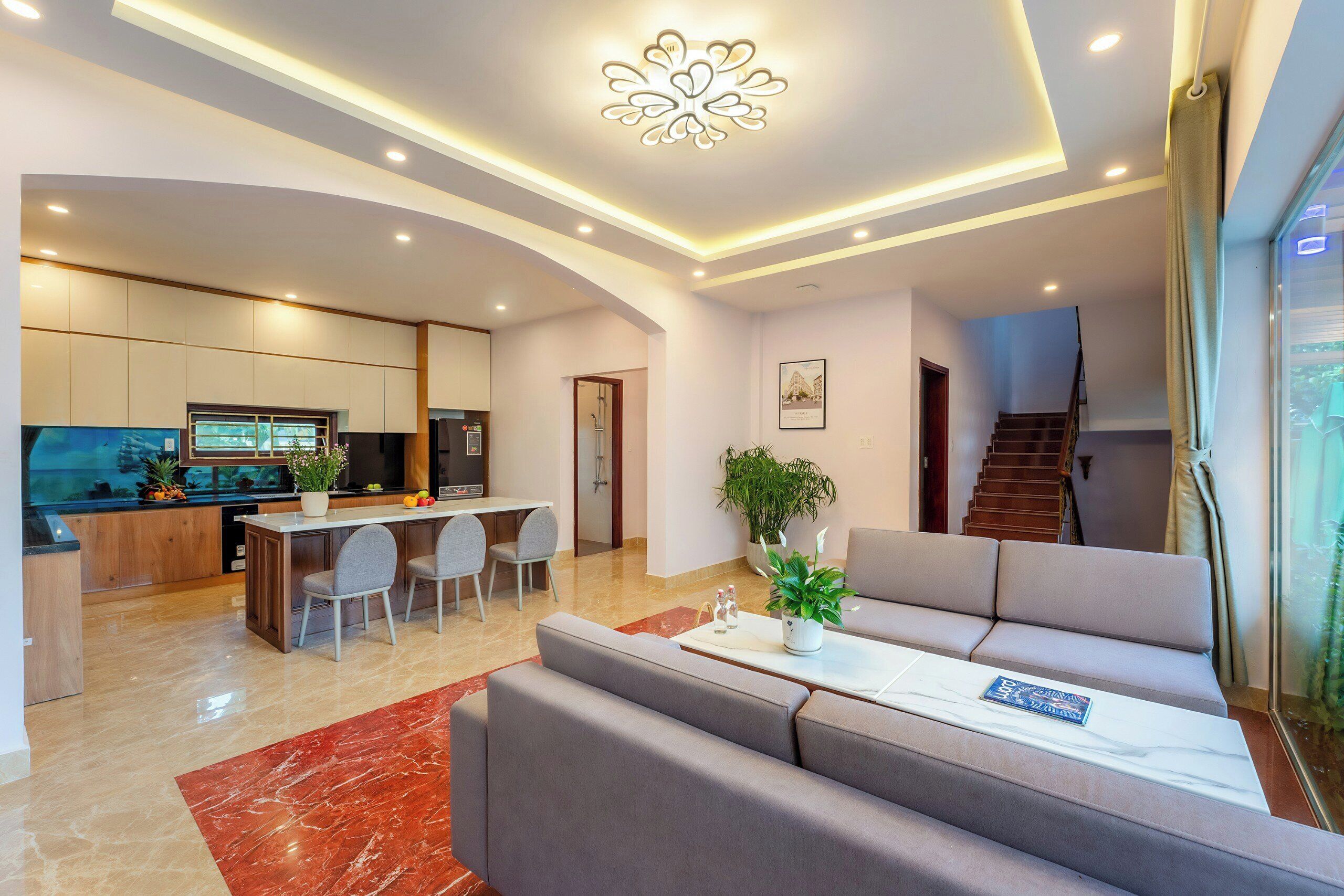 Una sala de estar moderna con un sofá, un comedor con sillas, una cocina con televisor y una escalera.