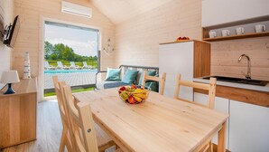 Interior de cabana de madeira com área de jantar, cozinha e vista para uma piscina.