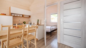 Quarto compacto e moderno, com decoração em madeira, cozinha compacta, área de refeições e uma cama.