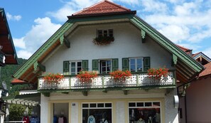 A traditional chalet with a balcony adorned with red flowers, a shop entrance, and a clear sky. - Ferienwohnung 3 für Max. 2 Personen (Ruhpolding)