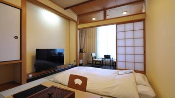 Een hotelkamer met een bed, een televisie, een bureau met stoel, en een verschuifbare shoji-scherm.