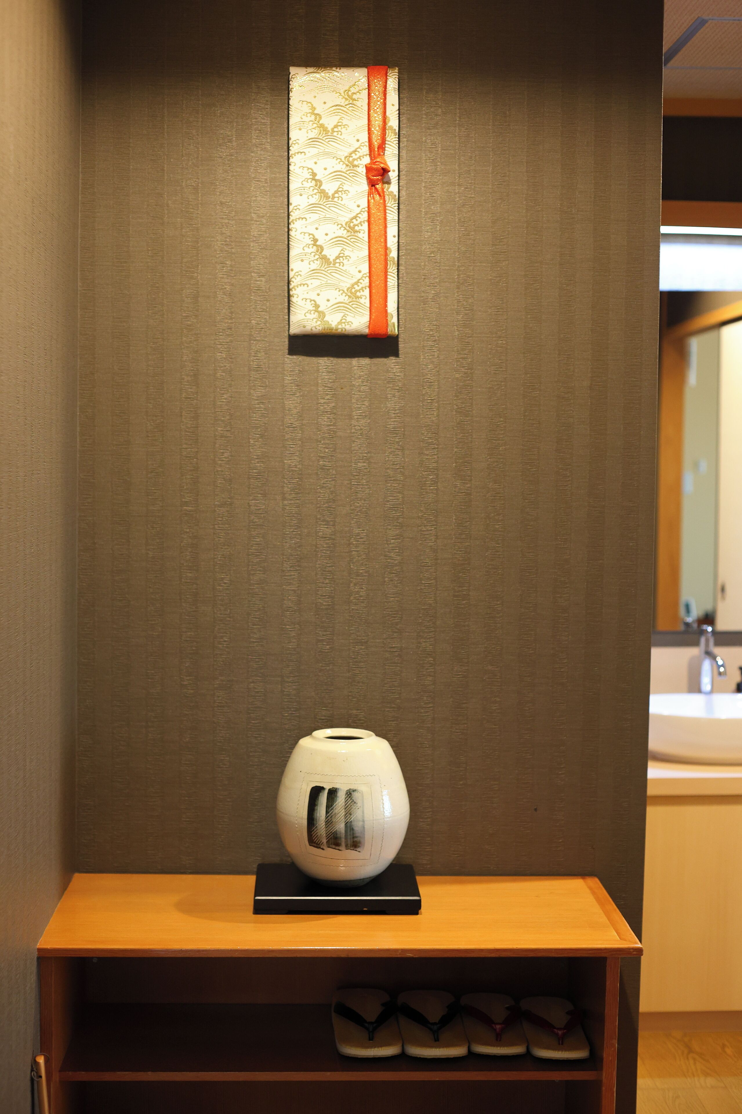 A wooden nightstand with a decorative vase and a framed artwork above it.