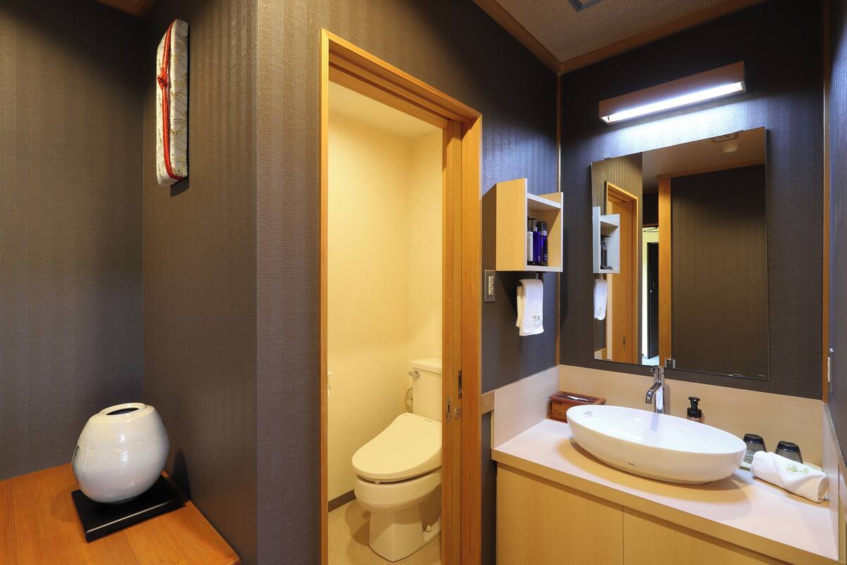 Une salle de bain moderne avec des toilettes blanches, un grand miroir et un meuble-lavabo en bois avec un évier.