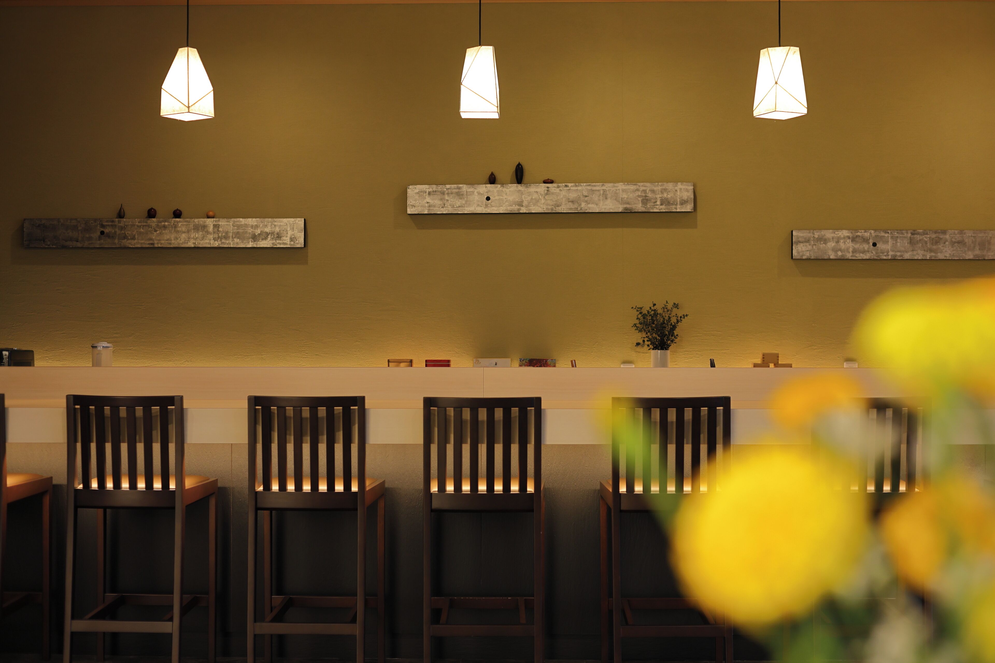 Un área de bar con sillas de madera, luces colgantes y un estante con adornos.