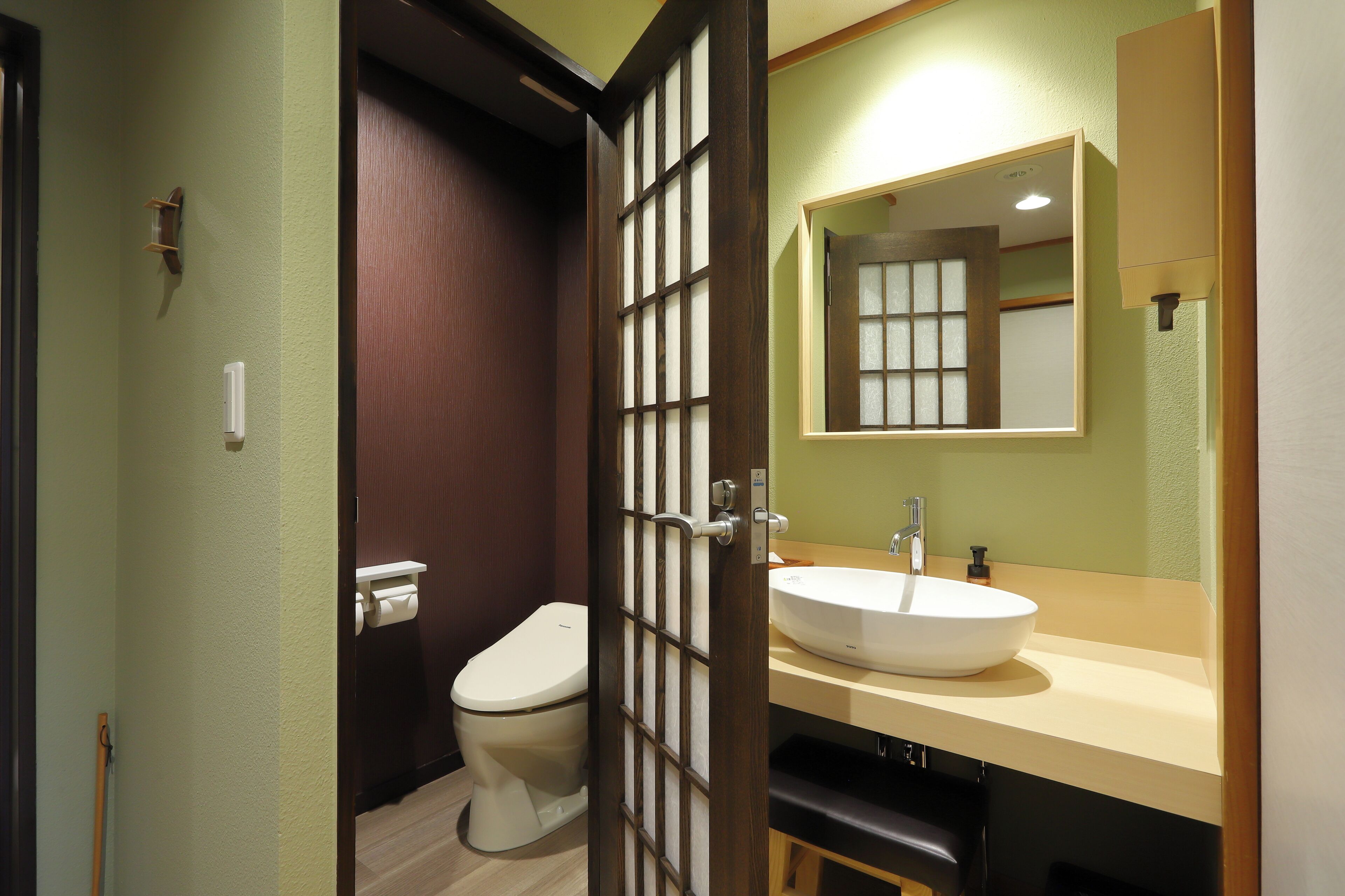 A bathroom with a toilet, sink, mirror, and wooden door.