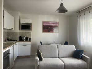 A compact kitchen with a microwave, coffee maker, and sink. There is a gray sofa with cushions and a painting on the wall. - Au Calme et Proche Centre-ville, Studio Rénové Avec Équipements Neufs et Parking (Gap)