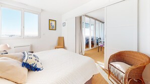 Un dormitorio con cama, una silla, una ventana y un puertas corredera que da a un balcón.