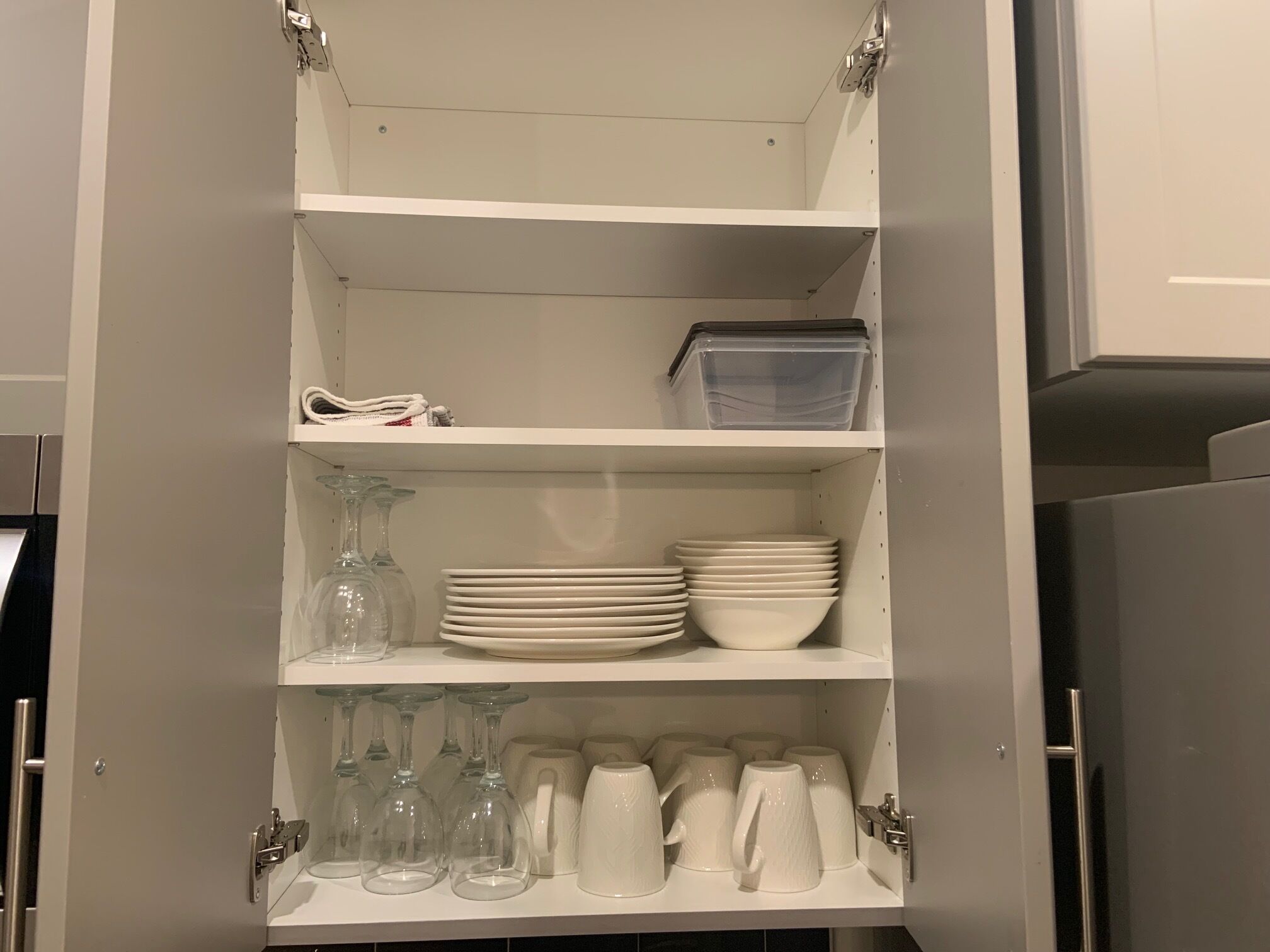 Un meuble blanc doté de plusieurs étagères, contenant des assiettes empilées, des bols, des verres à vin et un récipient en plastique.
