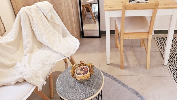 Una habitación moderna con un armario de madera, una mesa redonda con sillas, una pequeña mesa redonda con una cesta tejida y un espejo en la pared.
