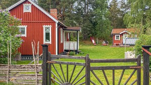 Een rood houten huis met een veranda, een klein rood gebouw op de achtergrond, en een houten hek.