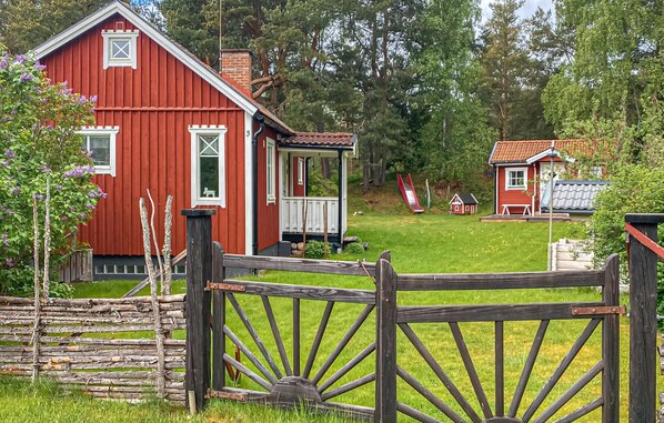 Een rood houten huis met een veranda, een klein rood gebouw op de achtergrond, en een houten hek.