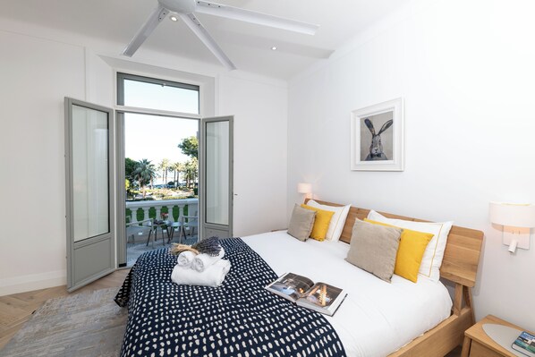 Habitación de hotel con una cama grande, vista a través de una puerta abierta, un cuadro en la pared y una mesita de noche con lámpara.