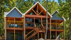 A two-story log cabin with a balcony, a staircase, and a view of the surrounding forest.