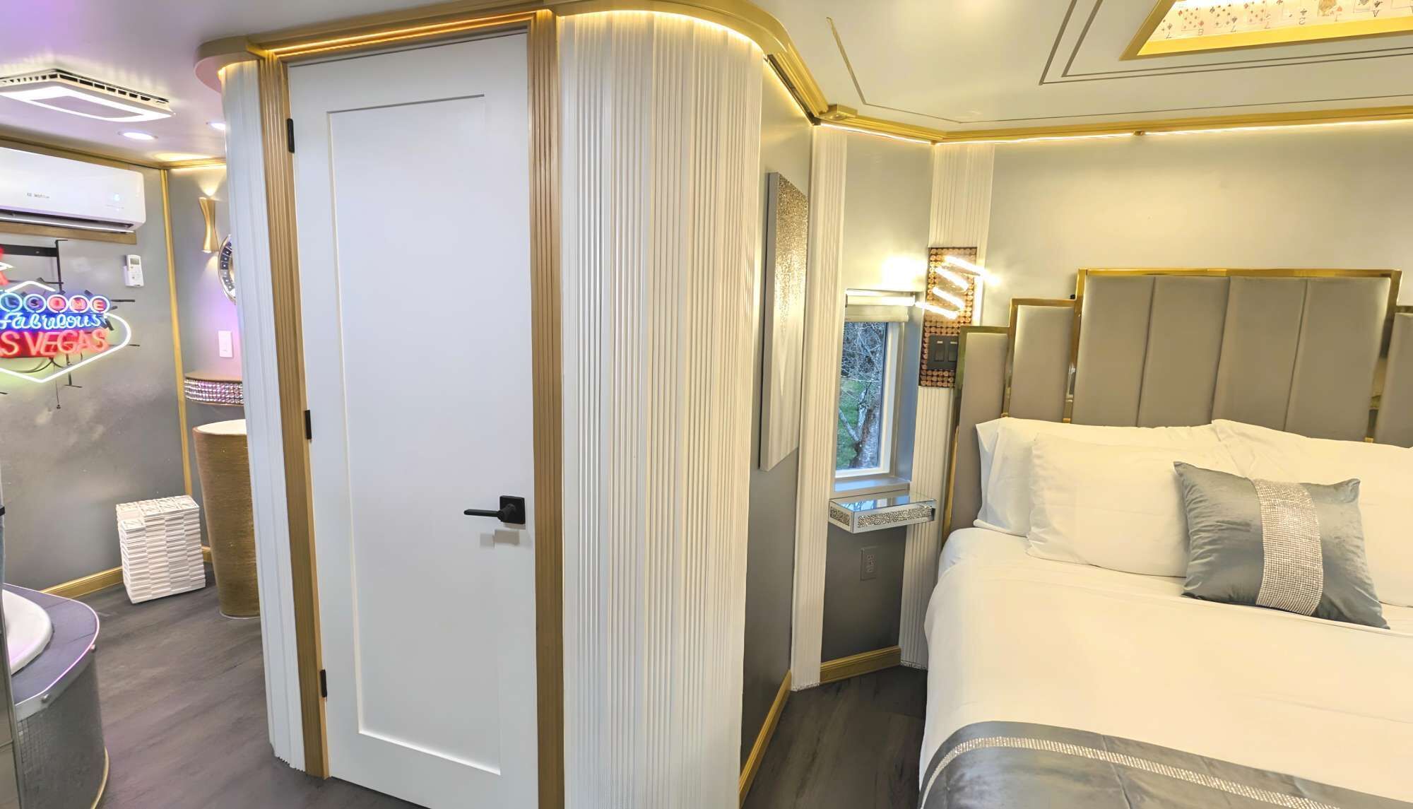 A hotel room with a bed, a bedside table, a mirror, and a door with a curtain.