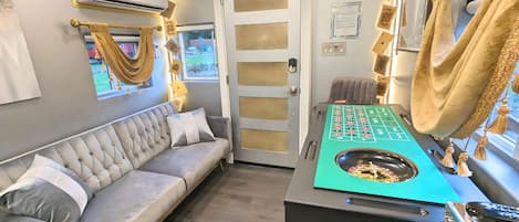 Ein Zimmer mit einer grauen Couch, einem Roulette-Tisch und einem Spieltisch für Kartenspiele.