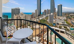 A balcony with a table and chairs overlooking a cityscape with tall buildings and a beach. - Surfers Paradise Unit (Level 10) (Surfers Paradise)