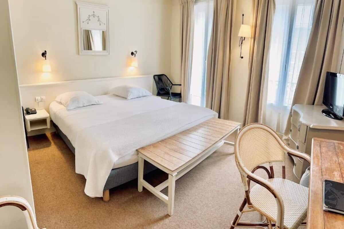 A hotel room with a bed, bedside table, lamp, chair, TV, and curtains.