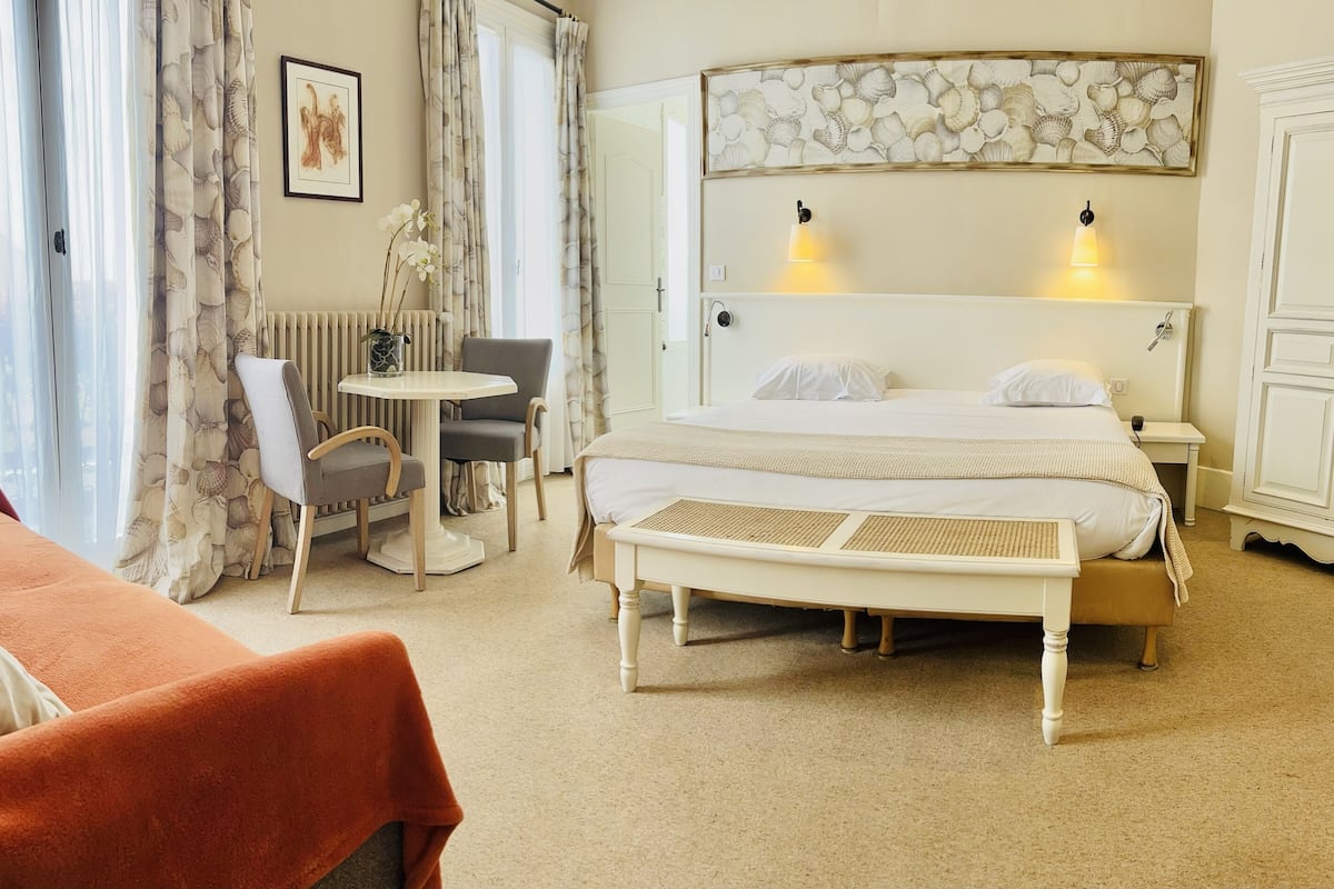 A hotel room with a bed, bedside table, chair, and a small table with a vase of flowers.