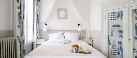 A neatly made bed with a tray of breakfast items, a bedside table with a lamp, and a window with curtains.