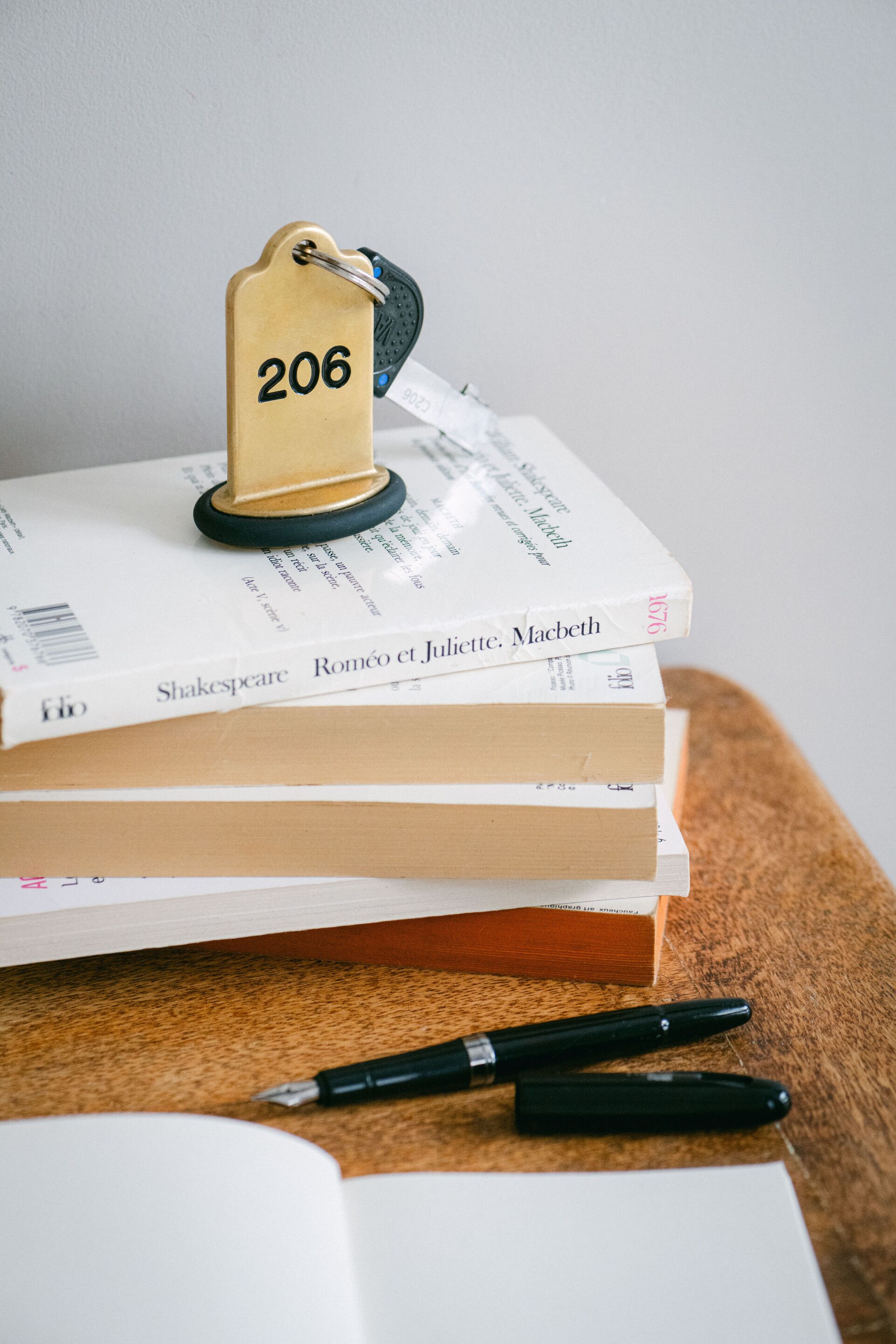 Una pila de libros con una etiqueta que dice "206" encima, un bolígrafo y un cuaderno abierto sobre una superficie de madera.