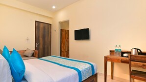 A bedroom with a bed, a wooden desk, a television, and a door. - Hotel The York (Noida)