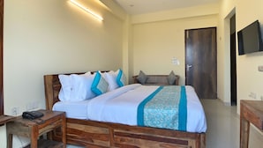 A bedroom with a wooden bed, bedside table, and a TV mounted on the wall. - Hotel The York (Noida)