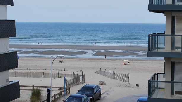 Uitzicht op een strand met een zandstrand, enkele geparkeerde auto's en een gebouw op de voorgrond.