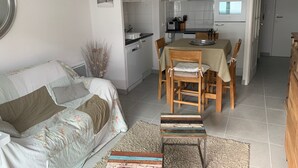 Een gezellig, ruimtelijk ingerichte leefruimte met een bank, een eettafel met stoelen, een keuken met apparatuur en een klein vloerkleed.
