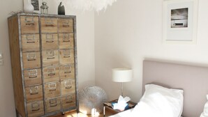 Een slaapkamer met een bed, nachtkastje, lamp, decoratieve ventilator en een houten kast met meerdere lades.