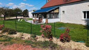 A house with a red roof, a covered patio, and a fenced yard with a lawn and shrubs.