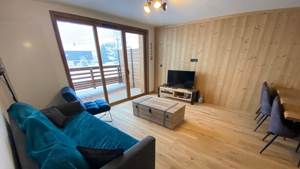 Un salon moderne comprenant un canapé, une table basse, un meuble pour la télévision et un coin repas avec des chaises.