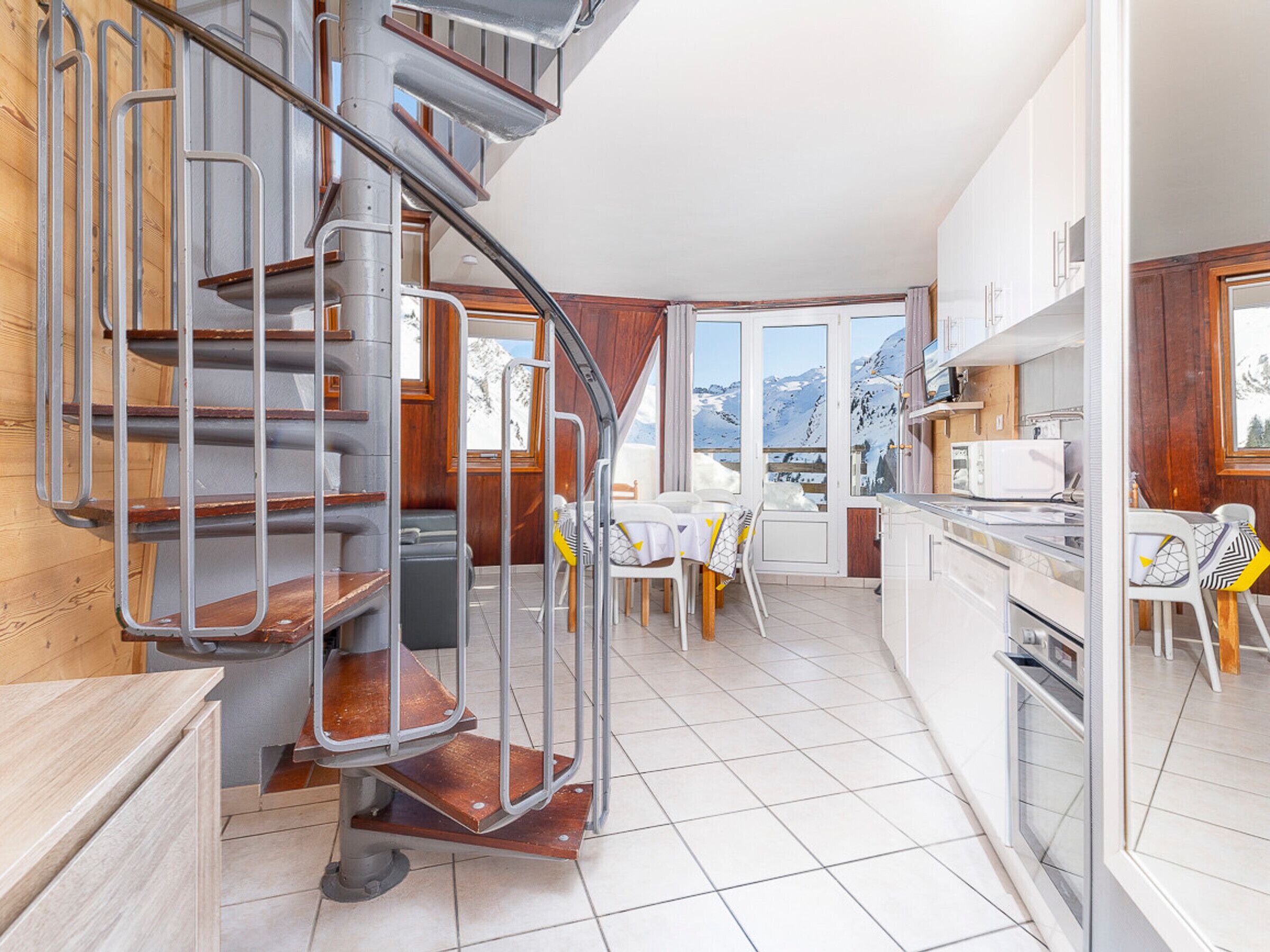 A compact kitchen with a built-in stove, a dining area with a table and chairs, and a spiral staircase leading to an upper level.