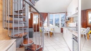 Une cuisine compacte dotée d’une cuisinière intégrée, un coin repas avec une table et des chaises, et un escalier en colimaçon menant à un niveau supérieur.