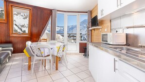 Une cuisine compacte avec un coin repas, un téléviseur fixé au-dessus du comptoir et une vue sur des montagnes enneigées par une grande fenêtre.