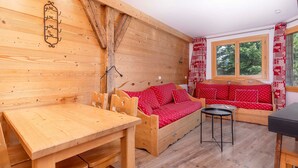 L'intérieur d'un chalet en bois accueillant, avec une table en bois, deux canapés rouges, une petite table ronde et une fenêtre donnant sur les arbres.