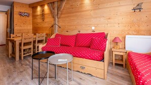 Une pièce chaleureuse avec un mur en bois, un canapé rouge orné de coussins à motifs de cœurs, une petite table ronde et une chaise en bois.