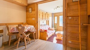 A cozy wooden room with a dining table and chairs, a bed with a quilt, and a wooden ladder.